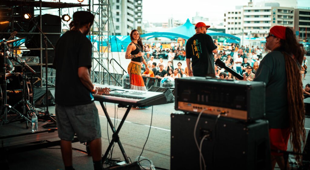 Shima Vibez performing live at an outdoor event in Okinawa, Japan, with the crowd in front of the stage.
